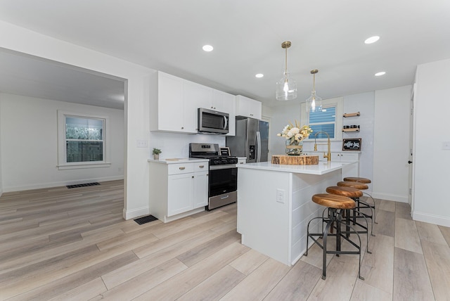 kitchen with light wood-type flooring, decorative light fixtures, a kitchen island, white cabinetry, and stainless steel appliances