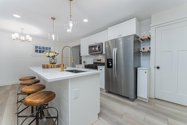 kitchen featuring white cabinetry, hanging light fixtures, an island with sink, light hardwood / wood-style floors, and appliances with stainless steel finishes