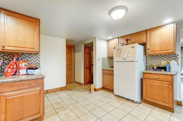 kitchen with tasteful backsplash, light stone countertops, light tile patterned floors, and white refrigerator