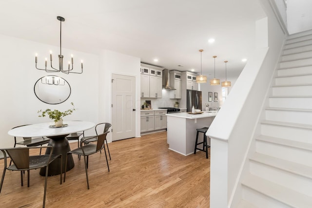 kitchen featuring white cabinetry, a breakfast bar area, stainless steel fridge, hanging light fixtures, and wall chimney exhaust hood