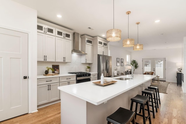 kitchen featuring an island with sink, sink, stainless steel fridge, wall chimney exhaust hood, and black gas range