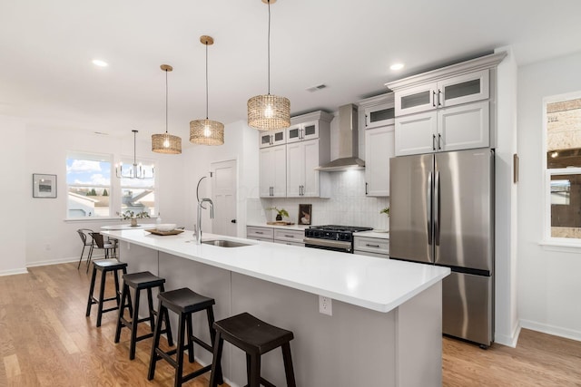 kitchen with stainless steel refrigerator, wall chimney exhaust hood, a kitchen island with sink, and range with gas cooktop