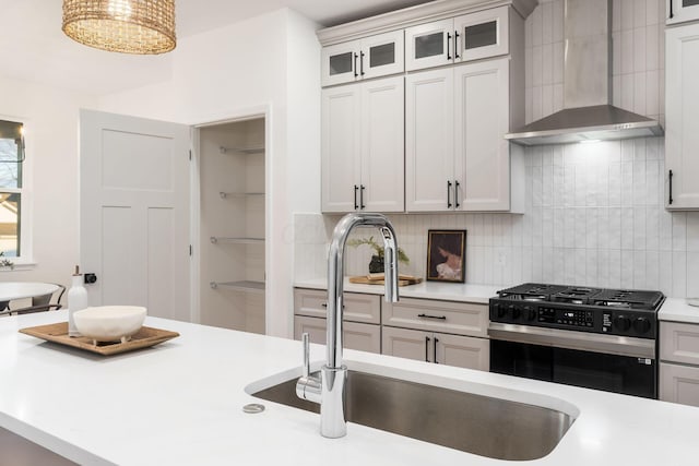 kitchen featuring wall chimney exhaust hood, black range with gas cooktop, sink, and white cabinets