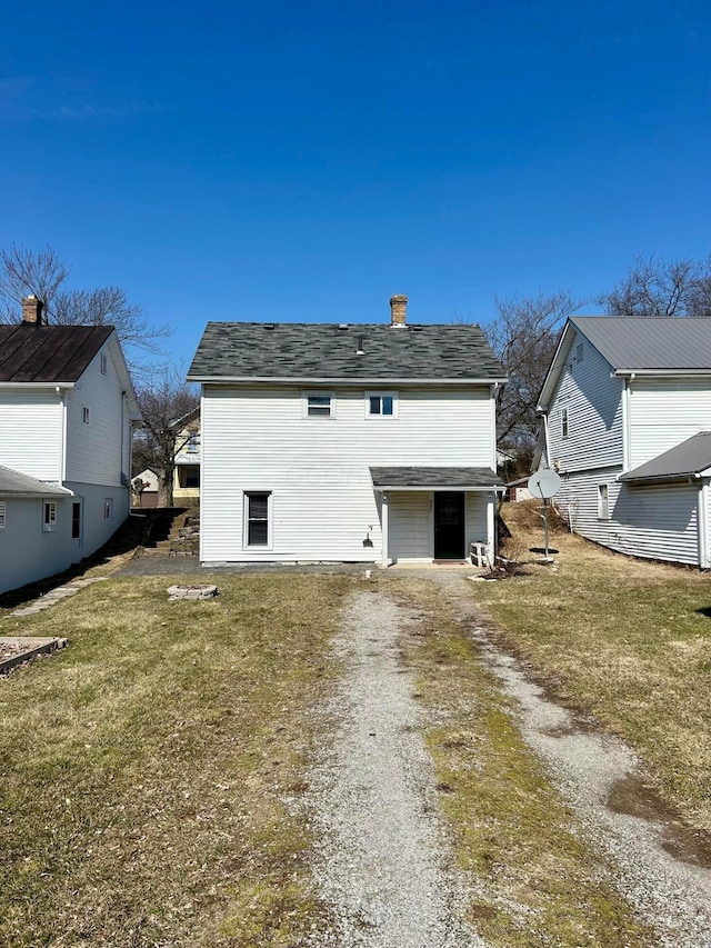 back of property featuring a lawn, a chimney, and driveway