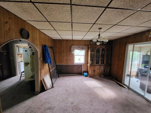 spare room featuring wood walls, carpet, and a notable chandelier