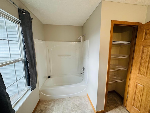 bathroom with a textured ceiling, shower / tub combination, and baseboards