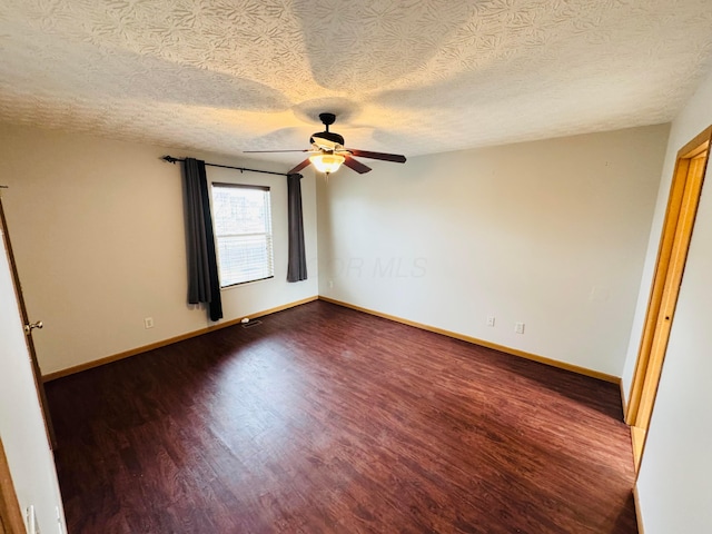 spare room featuring dark wood-style floors, ceiling fan, a textured ceiling, and baseboards