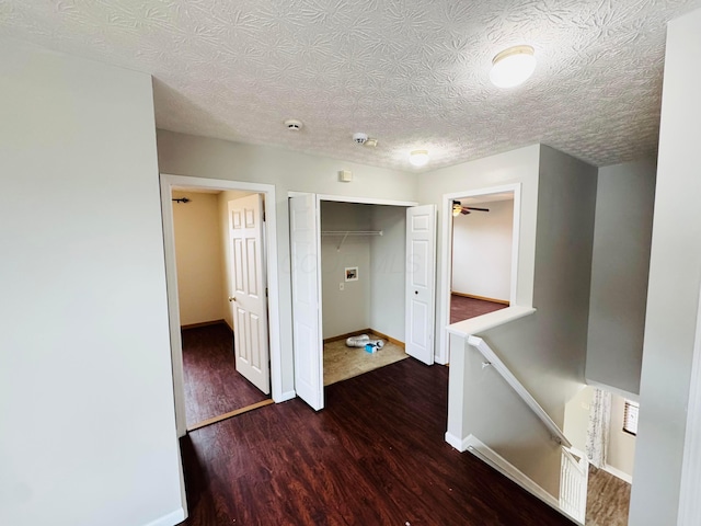 corridor featuring a textured ceiling, wood finished floors, an upstairs landing, and baseboards