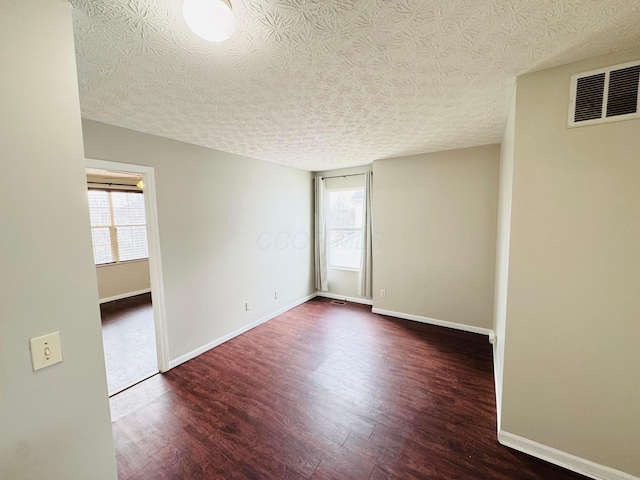 unfurnished room featuring a healthy amount of sunlight, visible vents, baseboards, and wood finished floors