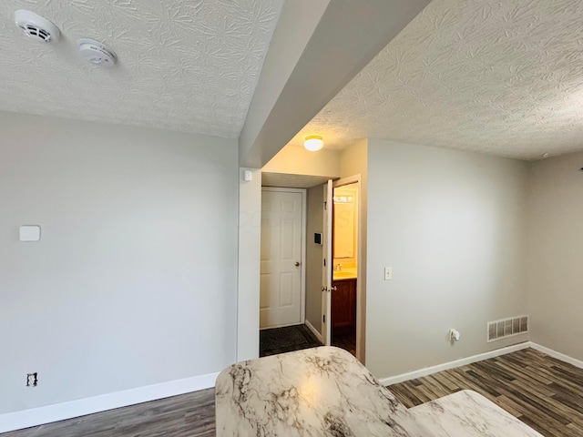 bedroom featuring dark wood-style floors, a textured ceiling, visible vents, and baseboards