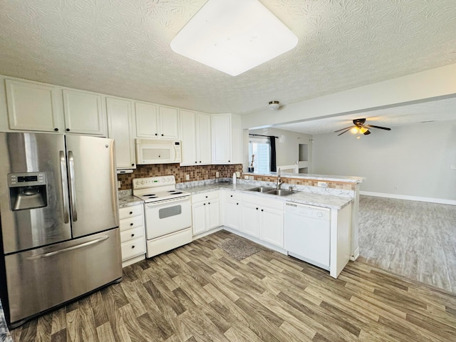 kitchen featuring a peninsula, white appliances, a sink, and light wood-style flooring