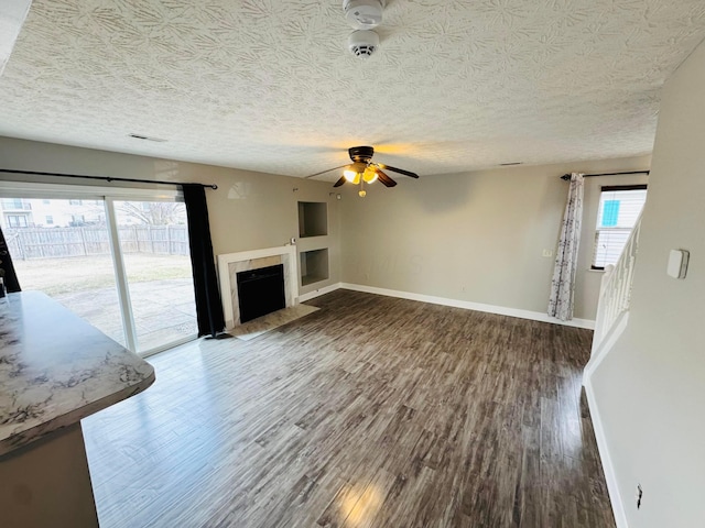 unfurnished living room with a textured ceiling, a fireplace, baseboards, and wood finished floors