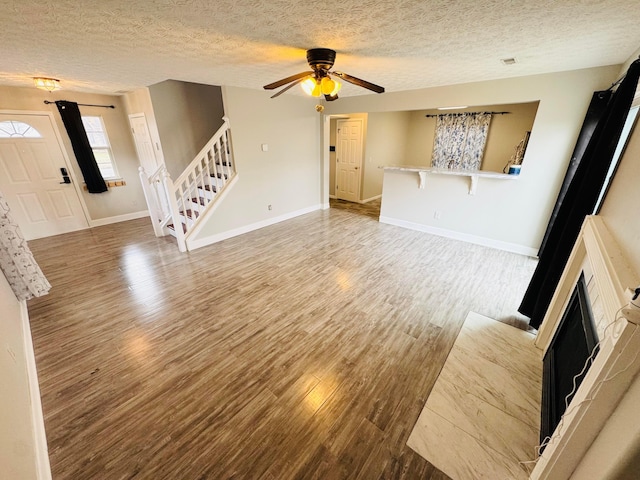 unfurnished living room featuring a textured ceiling, a fireplace, wood finished floors, baseboards, and stairs