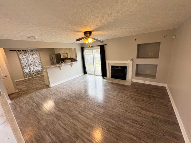 unfurnished living room featuring baseboards, a fireplace with flush hearth, ceiling fan, wood finished floors, and a textured ceiling