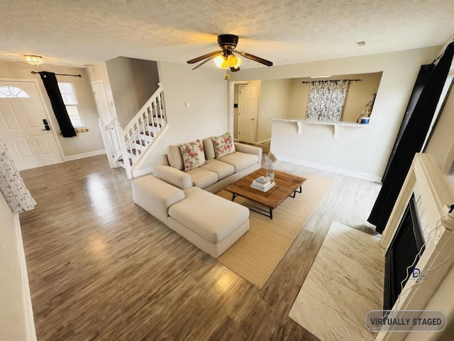 unfurnished living room featuring a textured ceiling, wood finished floors, stairs, and baseboards