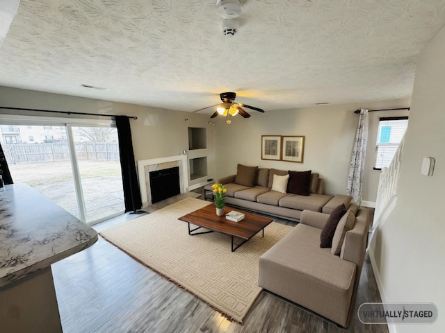 living room with a textured ceiling, wood finished floors, a fireplace with flush hearth, a ceiling fan, and baseboards