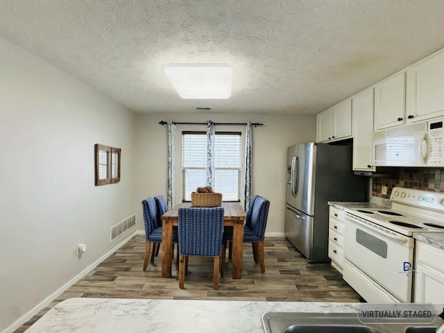 kitchen with white appliances, wood finished floors, visible vents, and white cabinets