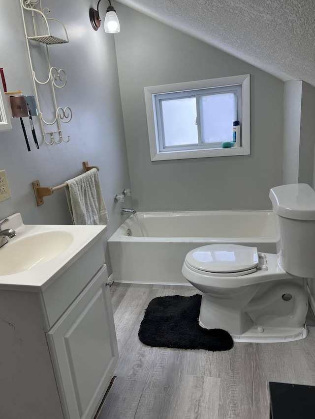 bathroom featuring toilet, hardwood / wood-style flooring, a textured ceiling, a bathtub, and vanity