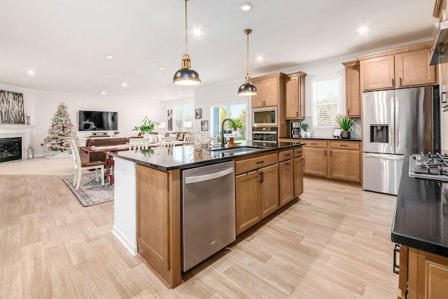 kitchen featuring sink, light hardwood / wood-style floors, pendant lighting, a kitchen island with sink, and appliances with stainless steel finishes