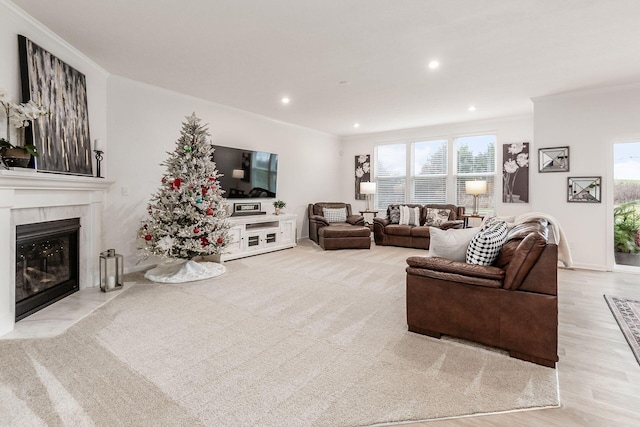 living room with a tiled fireplace, crown molding, a wealth of natural light, and light hardwood / wood-style flooring