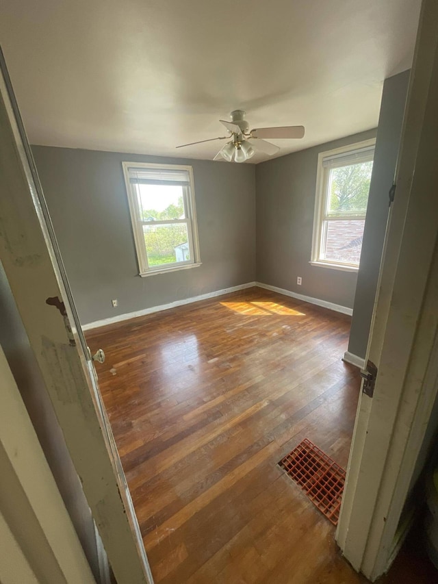 unfurnished room featuring a wealth of natural light, dark wood-type flooring, and ceiling fan