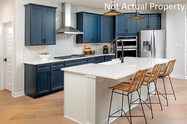 kitchen with wall chimney range hood, a breakfast bar area, blue cabinetry, and stainless steel appliances