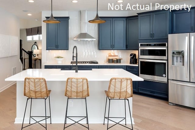 kitchen with a kitchen bar, blue cabinetry, stainless steel appliances, and wall chimney exhaust hood