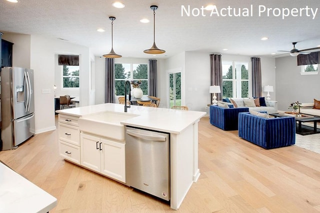 kitchen with a sink, stainless steel appliances, light countertops, light wood-style floors, and pendant lighting