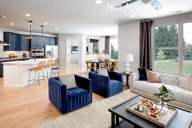 living area featuring baseboards, visible vents, light wood-style flooring, recessed lighting, and a textured ceiling