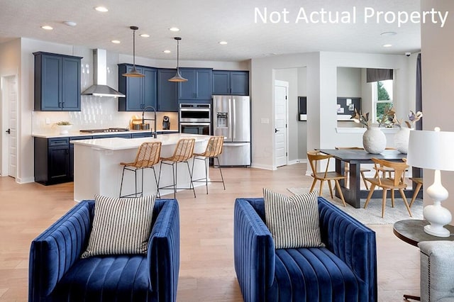 kitchen with stainless steel appliances, light countertops, a kitchen bar, wall chimney exhaust hood, and open floor plan