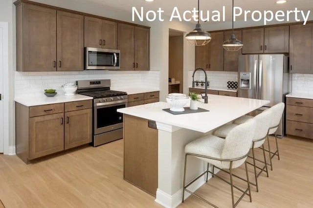 kitchen with backsplash, light countertops, a kitchen breakfast bar, appliances with stainless steel finishes, and light wood-style floors