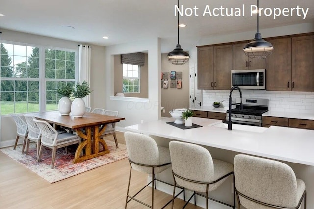 kitchen with light wood-type flooring, decorative light fixtures, stainless steel appliances, light countertops, and decorative backsplash