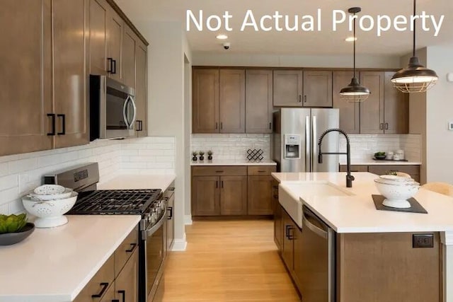 kitchen with an island with sink, a sink, stainless steel appliances, light countertops, and light wood-style floors