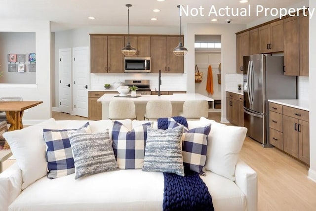 kitchen with backsplash, a center island with sink, light countertops, stainless steel appliances, and a sink