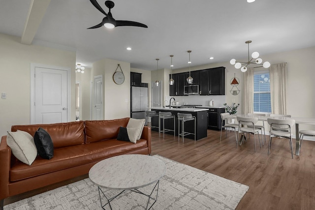 living room with beam ceiling, hardwood / wood-style floors, ceiling fan with notable chandelier, and sink