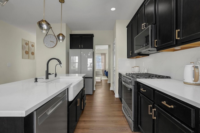 kitchen with appliances with stainless steel finishes, sink, decorative light fixtures, hardwood / wood-style flooring, and a center island with sink