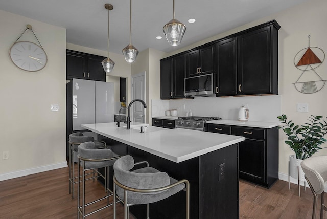 kitchen featuring a breakfast bar, stainless steel appliances, decorative light fixtures, dark hardwood / wood-style floors, and an island with sink