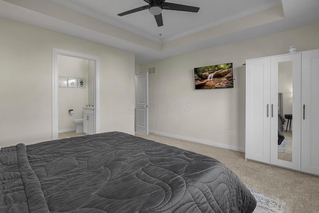 carpeted bedroom with ceiling fan, ornamental molding, connected bathroom, and a tray ceiling