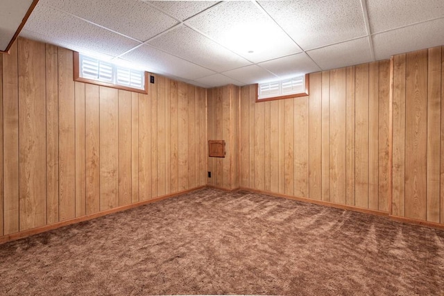 basement featuring a drop ceiling, carpet floors, and wooden walls