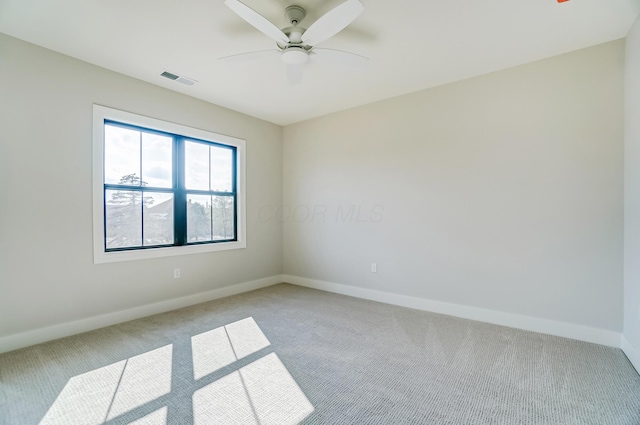 empty room featuring a ceiling fan, light colored carpet, visible vents, and baseboards