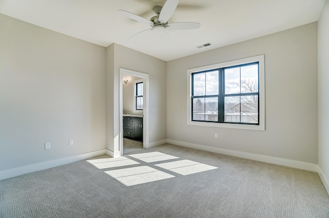 unfurnished bedroom featuring baseboards, visible vents, connected bathroom, a ceiling fan, and light colored carpet