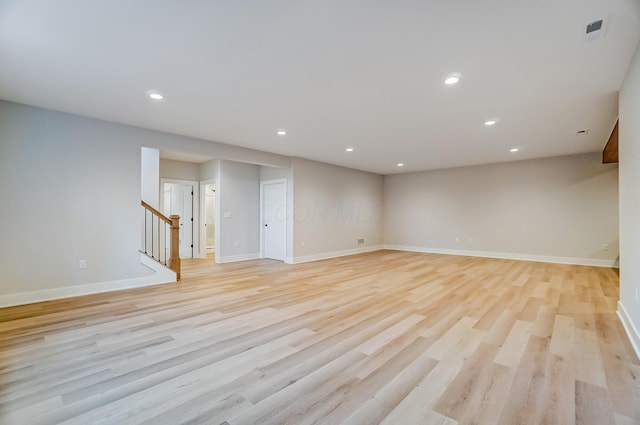 unfurnished room featuring light wood finished floors, stairway, visible vents, and baseboards