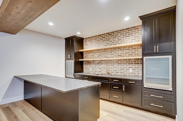 kitchen with open shelves, a sink, dark brown cabinetry, and light wood-style floors