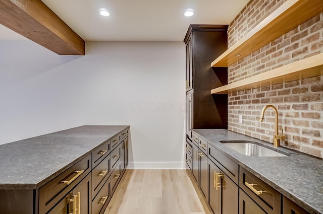 kitchen with baseboards, brick wall, light wood-style floors, open shelves, and a sink