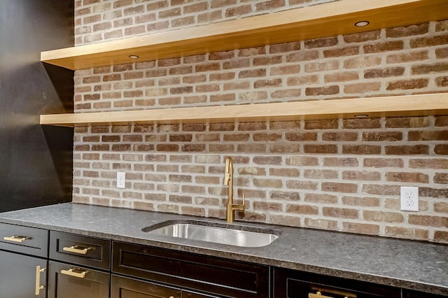 kitchen featuring open shelves, dark countertops, dark brown cabinetry, a sink, and brick wall