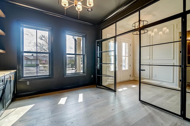 doorway featuring an inviting chandelier, light wood-style flooring, visible vents, and crown molding