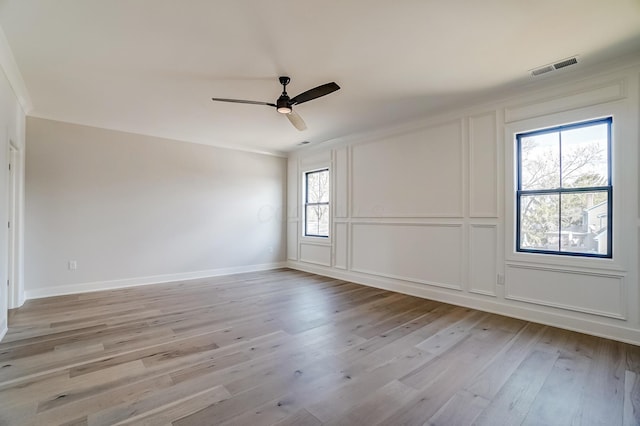 empty room featuring visible vents, a decorative wall, light wood-style flooring, ceiling fan, and baseboards