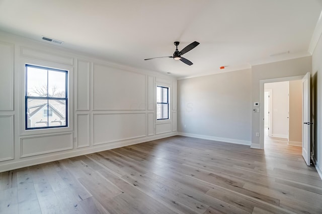 spare room featuring light wood-style flooring, a decorative wall, a ceiling fan, visible vents, and crown molding