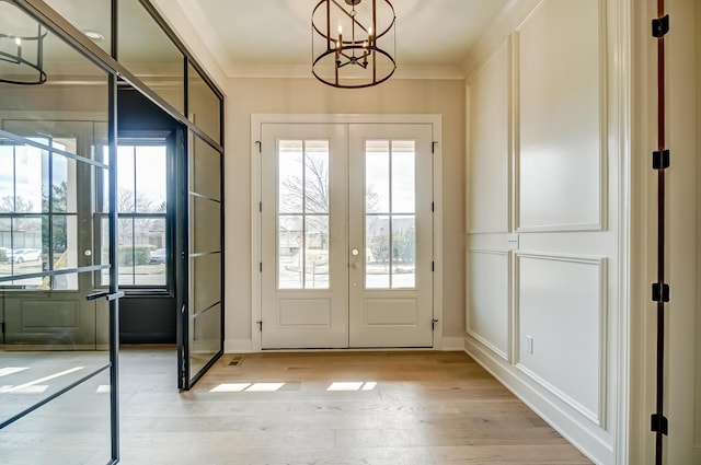 doorway to outside featuring a notable chandelier, french doors, light wood-type flooring, and crown molding