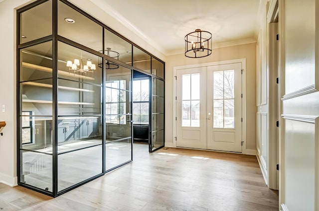 entryway featuring an inviting chandelier, wood finished floors, crown molding, and french doors